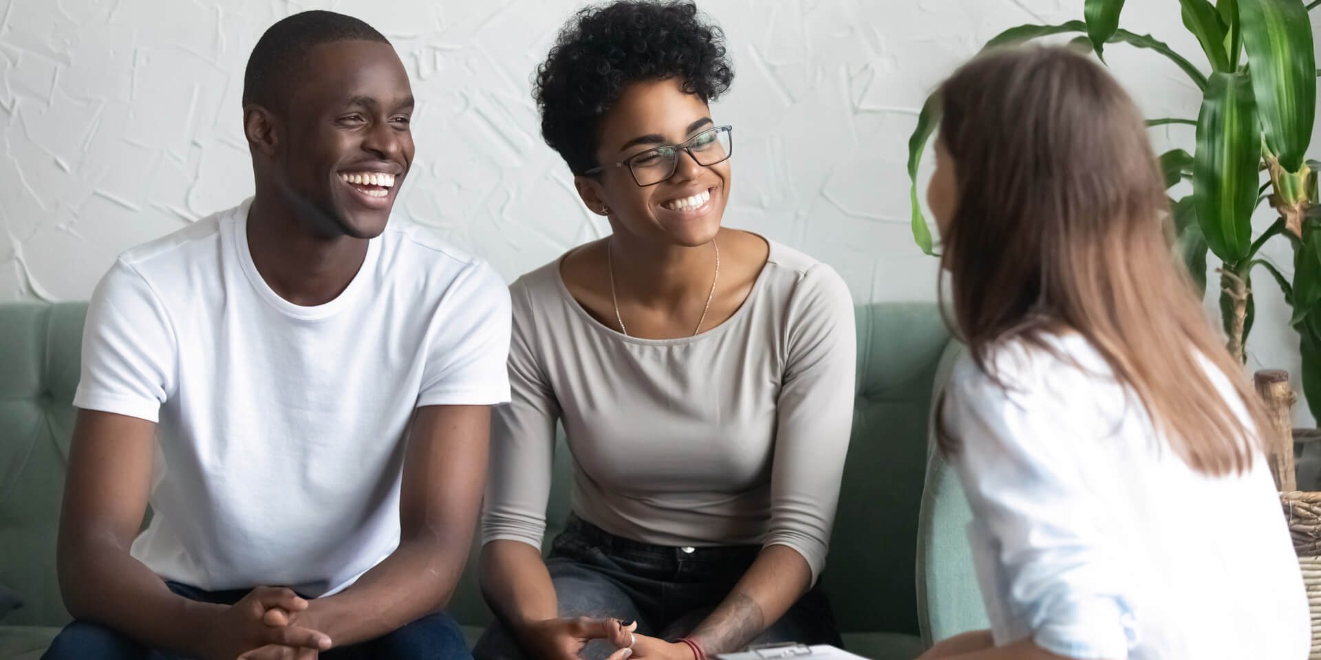 AdobeStock_239210822 Young couple smiling as they work with counselor in comfortable office setting